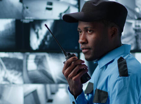 Side view of African-American security guard talk on radio in control room monitoring surveillance footage